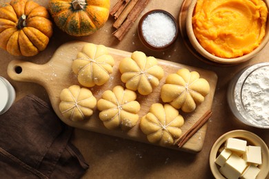 Photo of Raw pumpkin shaped buns and ingredients on brown table, flat lay