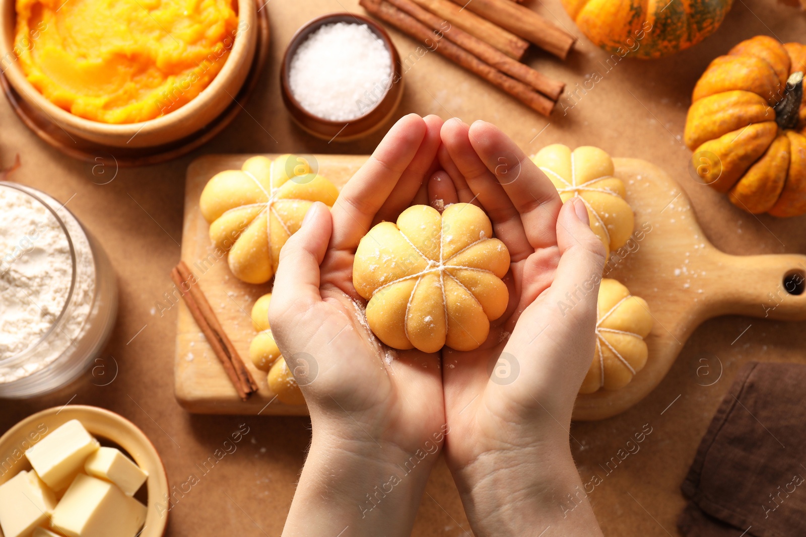 Photo of Woman making pumpkin shaped buns at brown table, top view