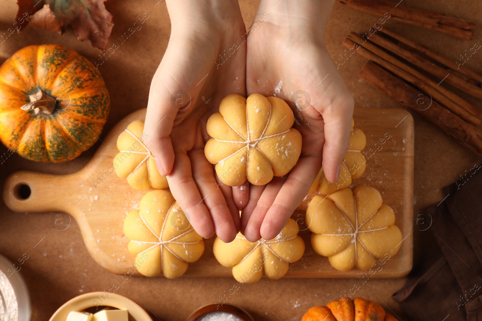 Photo of Woman making pumpkin shaped buns at brown table, top view