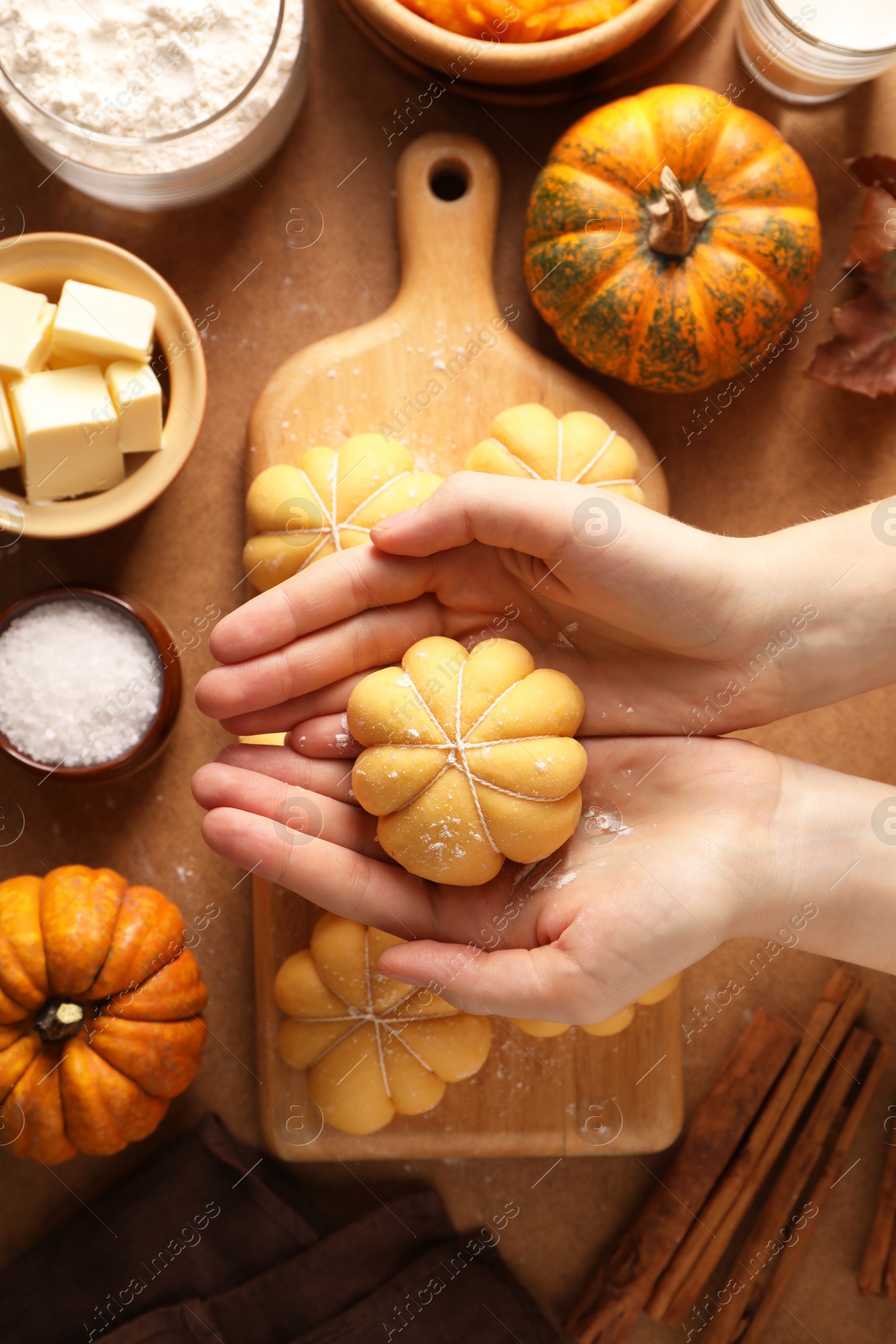 Photo of Woman making pumpkin shaped buns at brown table, top view