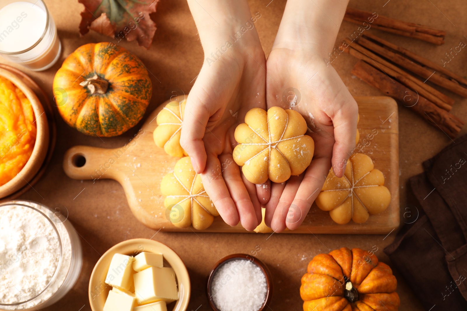 Photo of Woman making pumpkin shaped buns at brown table, top view