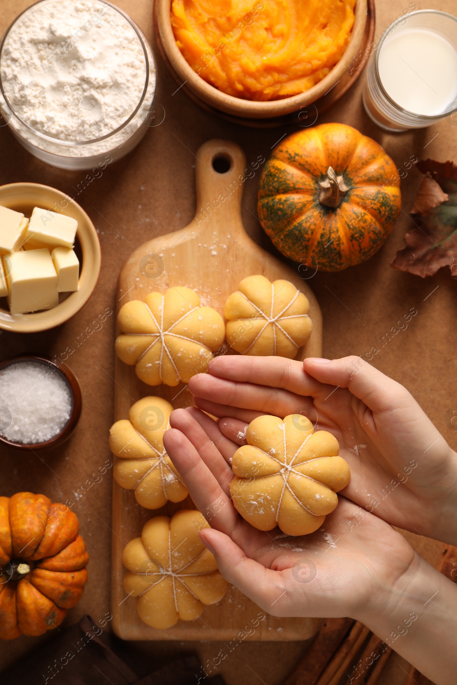 Photo of Woman making pumpkin shaped buns at brown table, top view