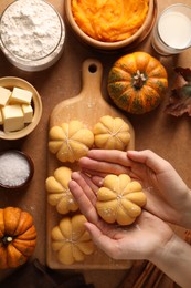 Photo of Woman making pumpkin shaped buns at brown table, top view