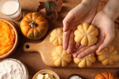 Photo of Woman making pumpkin shaped buns at brown table, top view