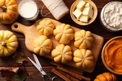 Photo of Raw pumpkin shaped buns and ingredients on wooden table, flat lay