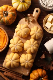 Photo of Raw pumpkin shaped buns and ingredients on wooden table, flat lay