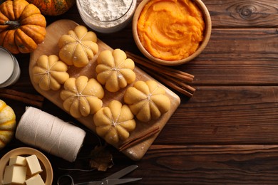 Photo of Raw pumpkin shaped buns and ingredients on wooden table, flat lay. Space for text