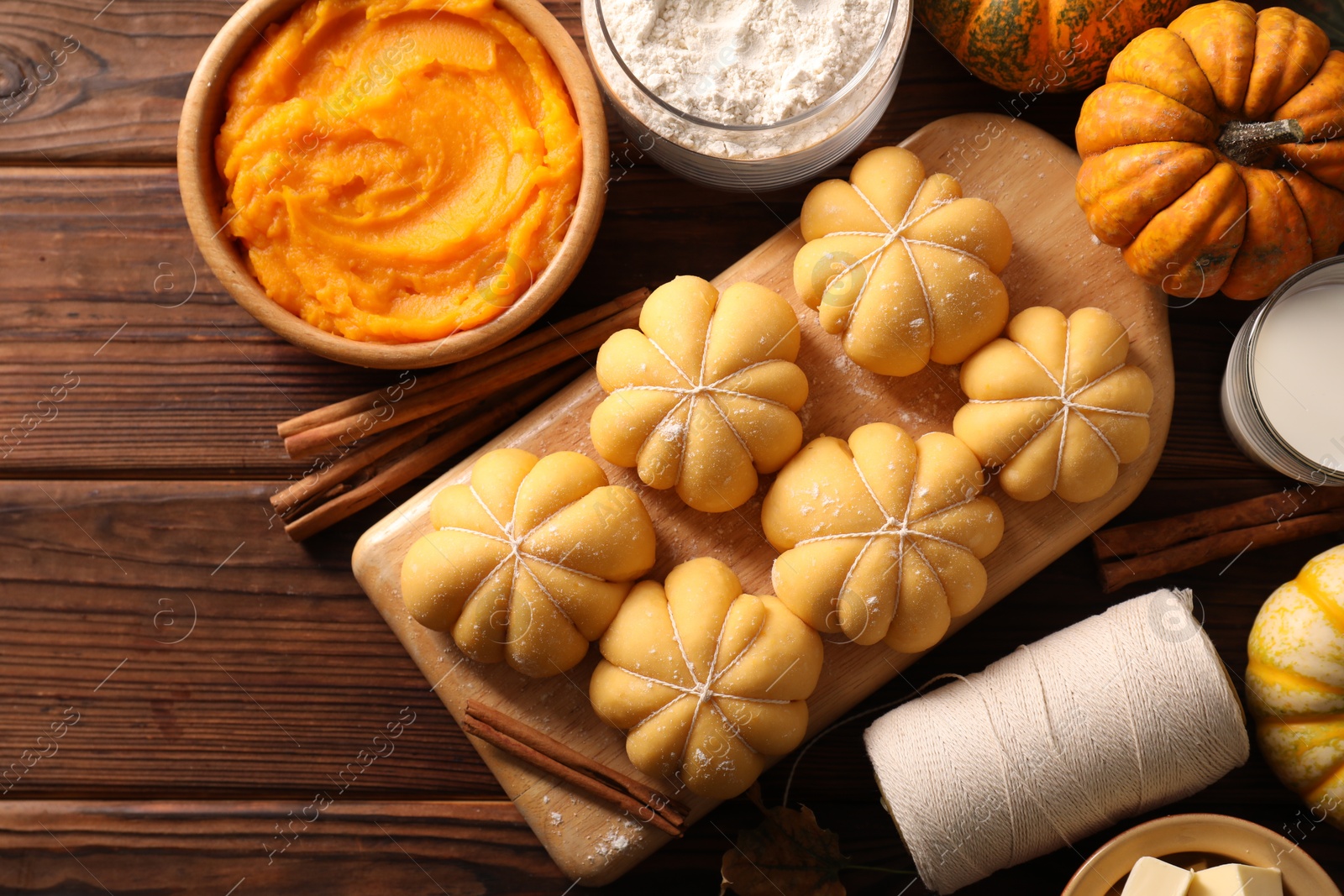 Photo of Raw pumpkin shaped buns and ingredients on wooden table, flat lay