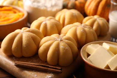 Photo of Raw pumpkin shaped buns and ingredients on wooden table, closeup