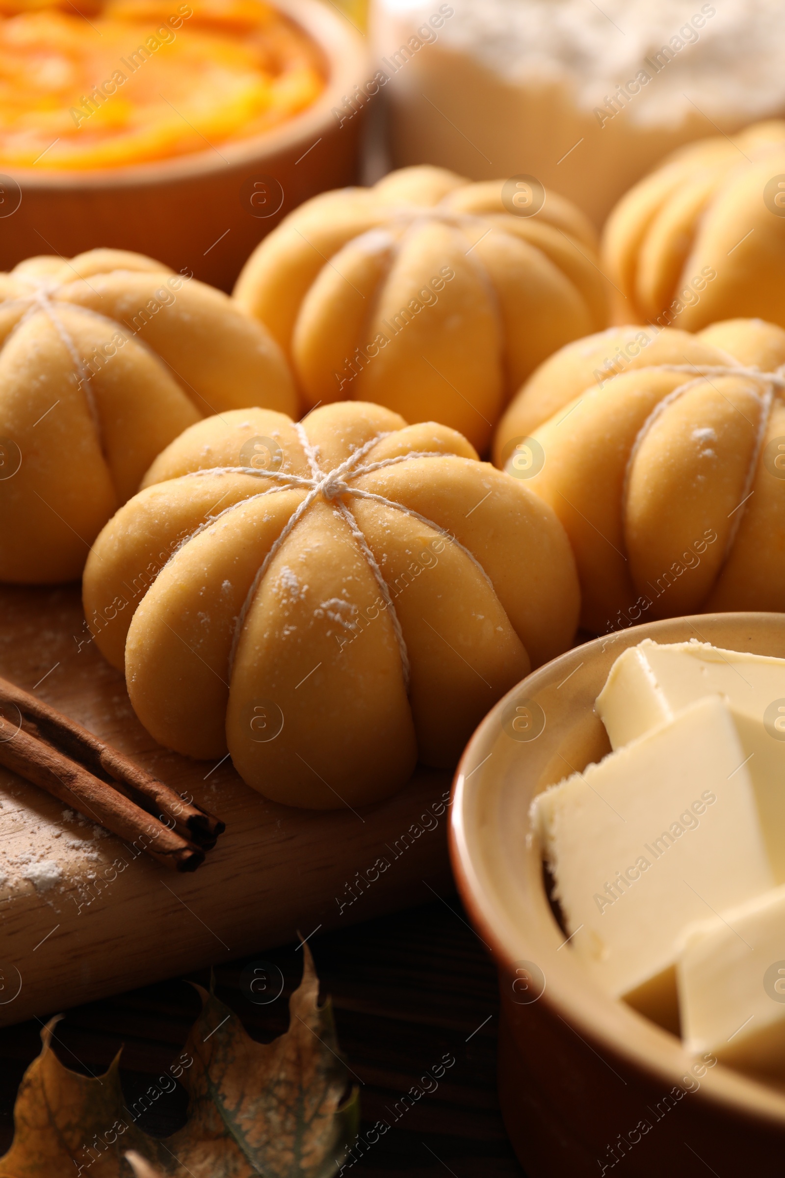 Photo of Raw pumpkin shaped buns and ingredients on wooden table, closeup