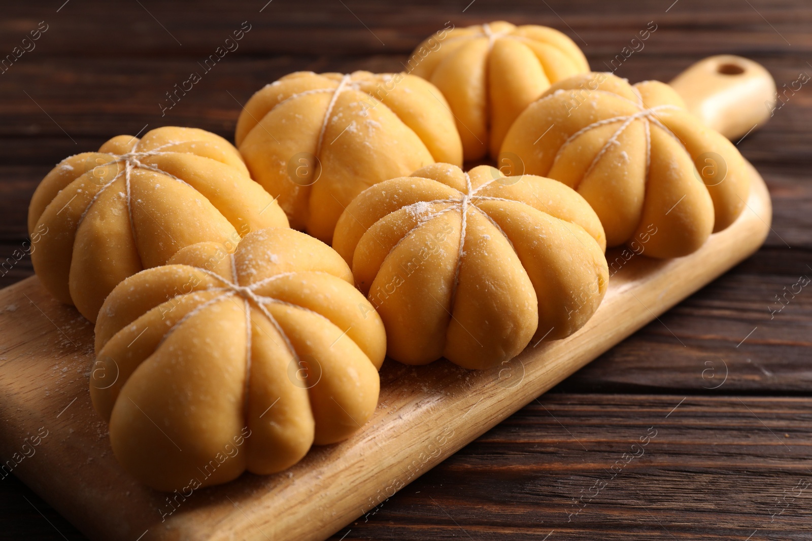 Photo of Raw pumpkin shaped buns on wooden table, closeup