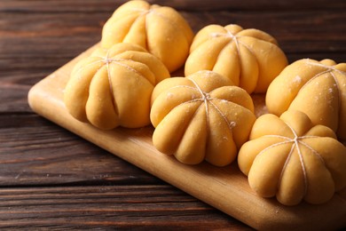 Photo of Raw pumpkin shaped buns on wooden table, closeup