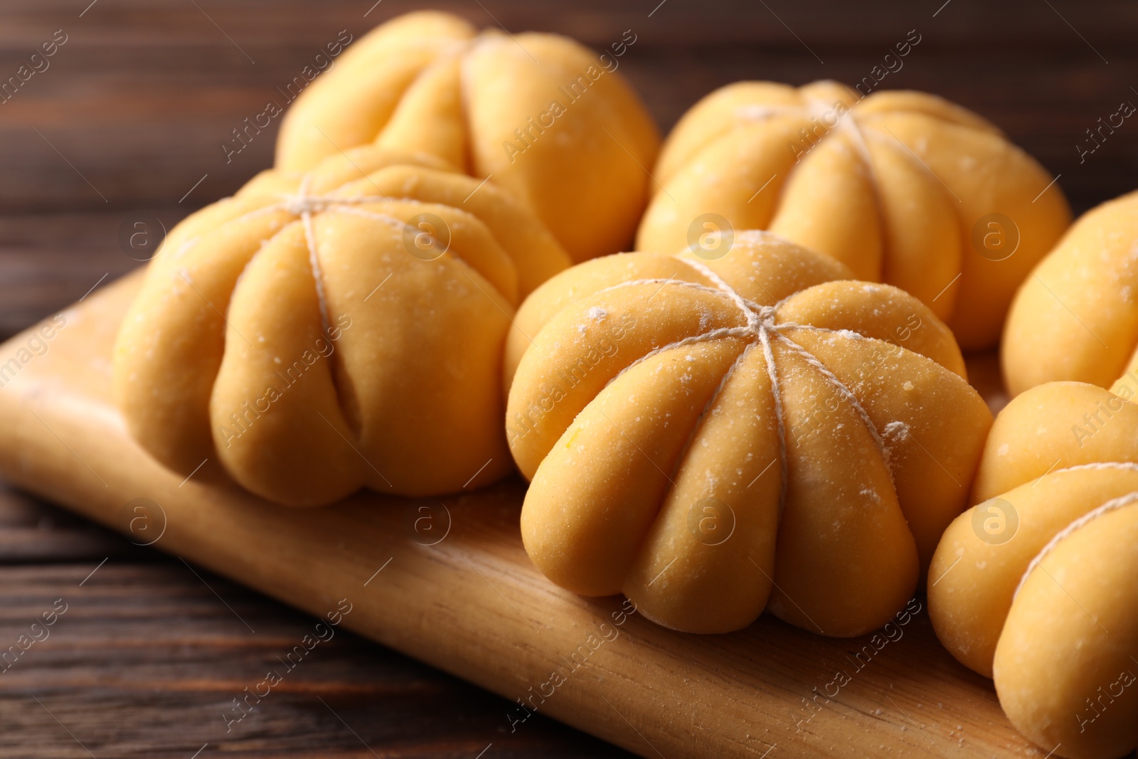 Photo of Raw pumpkin shaped buns on wooden table, closeup