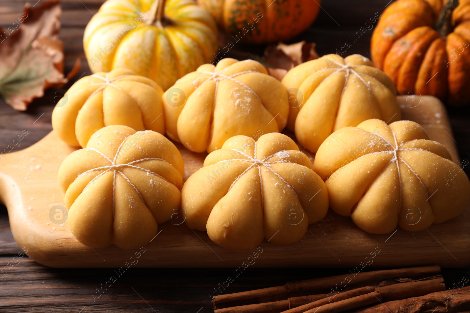 Photo of Raw pumpkin shaped buns and ingredients on wooden table, closeup