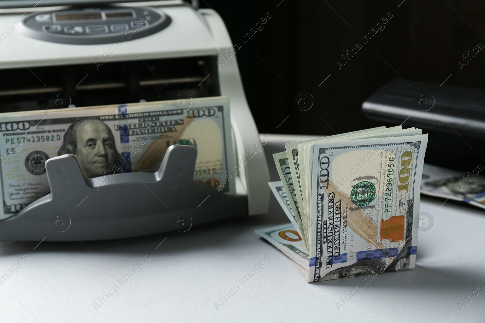 Photo of Dollar banknotes and money counter machine on light table, closeup