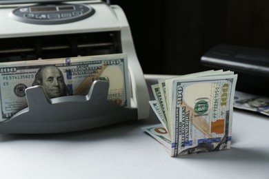 Dollar banknotes and money counter machine on light table, closeup