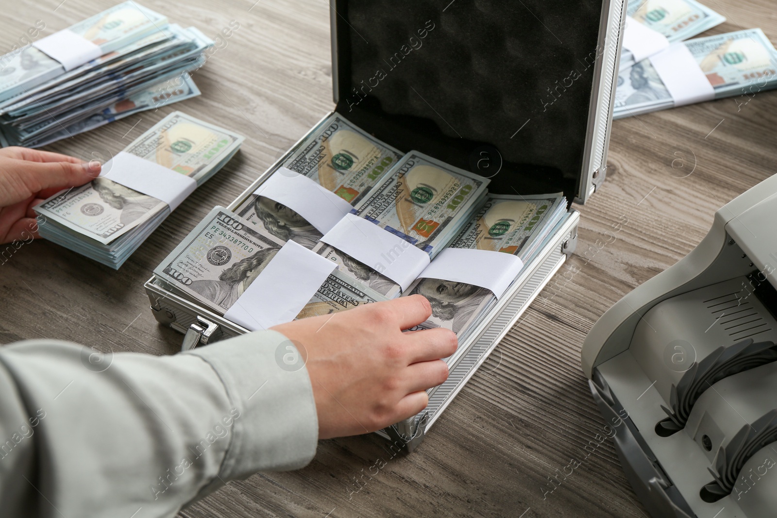 Photo of Woman counting dollar banknotes at wooden table, closeup