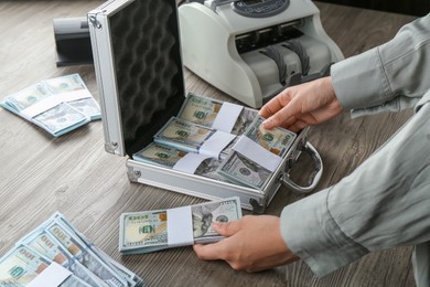 Photo of Woman counting dollar banknotes at wooden table, closeup