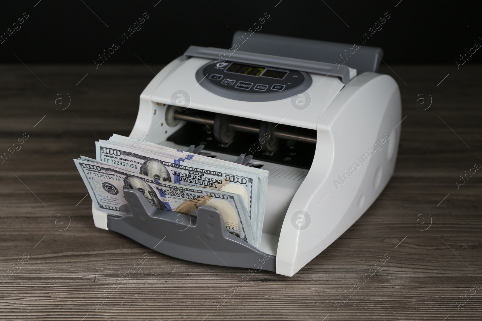 Photo of Money counter machine with dollar banknotes on wooden table