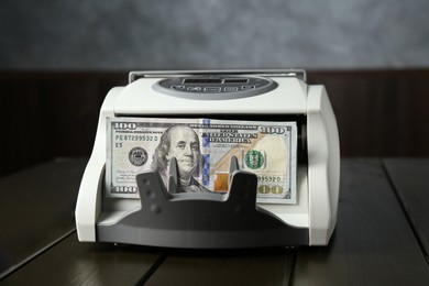 Photo of Money counter machine with dollar banknotes on wooden table