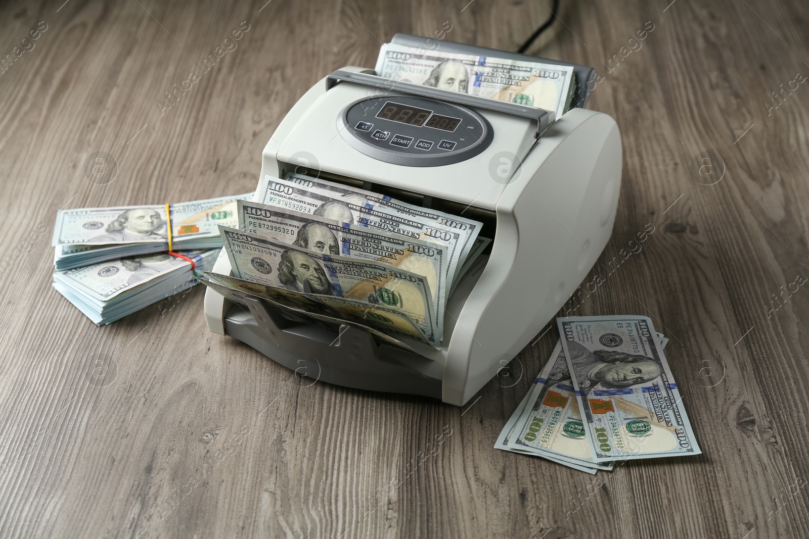 Photo of Money counter machine with dollar banknotes on wooden table