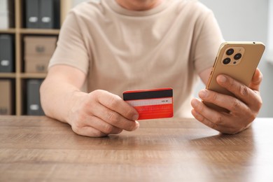 Photo of Man with credit card and smartphone at wooden table indoors, closeup