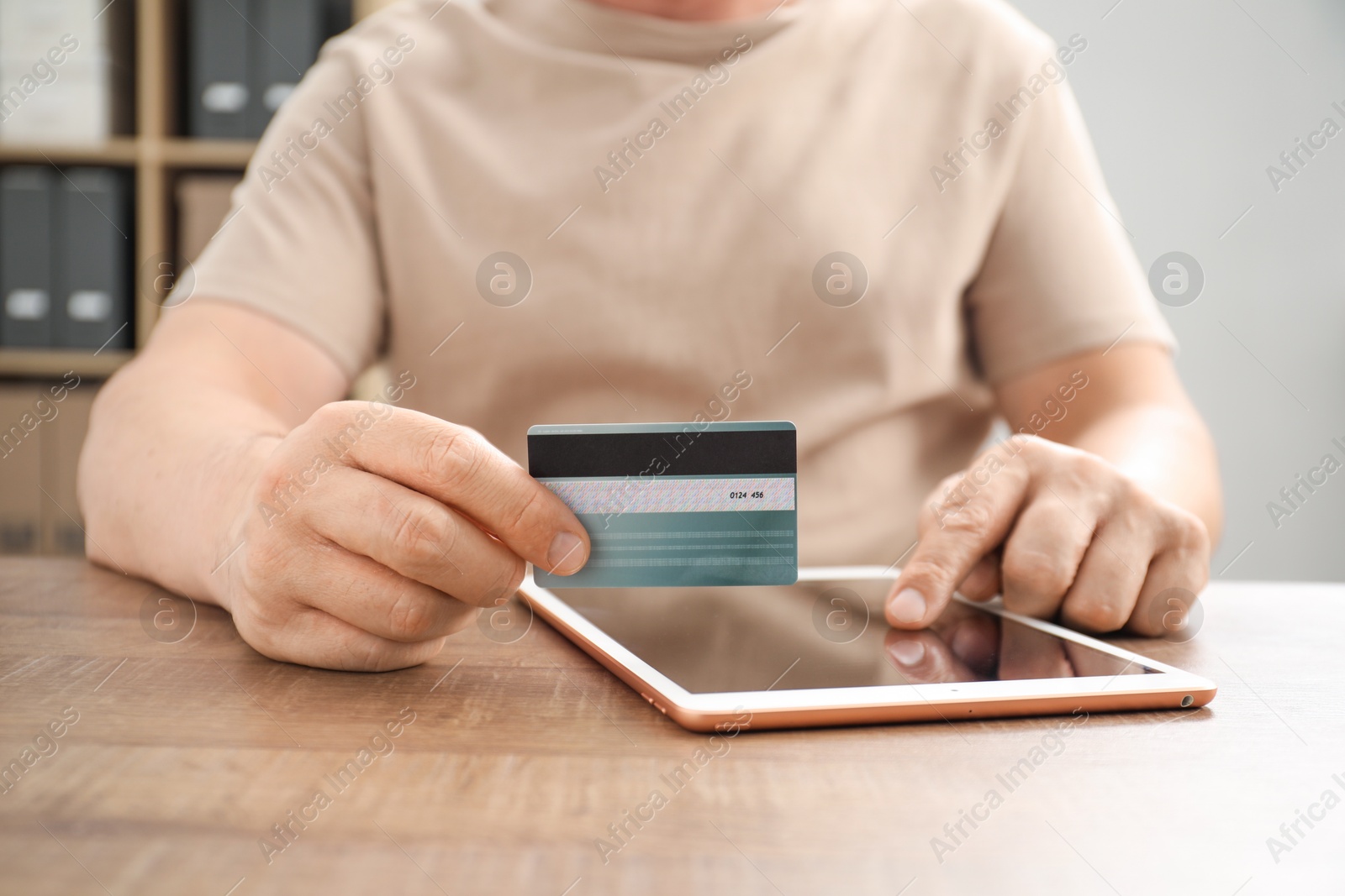 Photo of Man with credit card using tablet at wooden table indoors, closeup