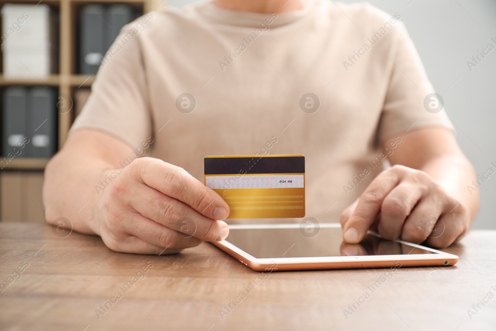 Photo of Man with credit card using tablet at wooden table indoors, closeup