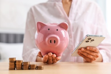 Photo of Woman with piggy bank and smartphone at table indoors, closeup