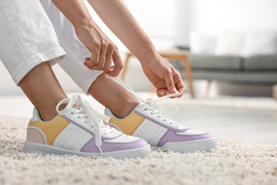 Photo of Woman tying shoelace of sneaker indoors, closeup