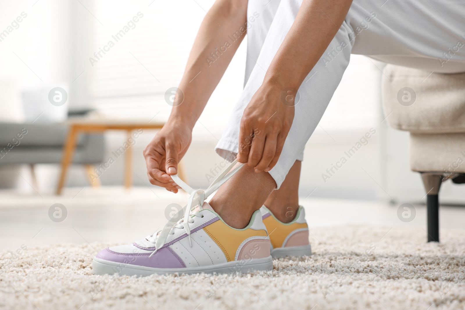 Photo of Woman tying shoelace of sneaker indoors, closeup