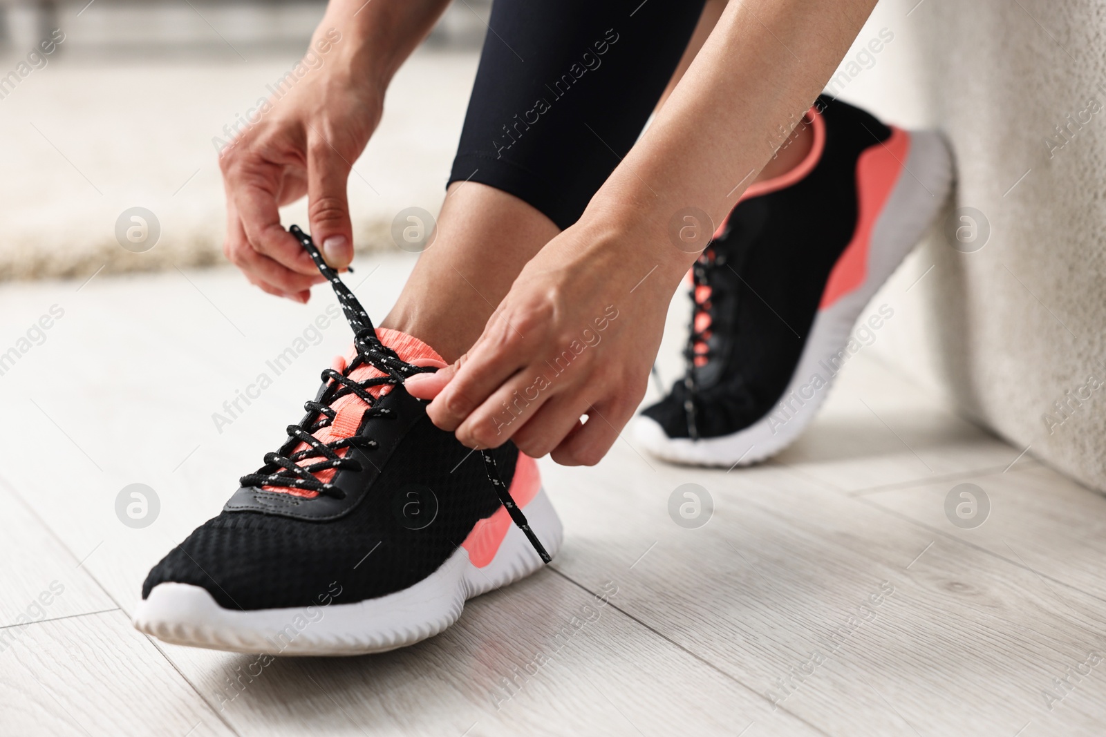 Photo of Woman tying shoelace of sneaker indoors, closeup