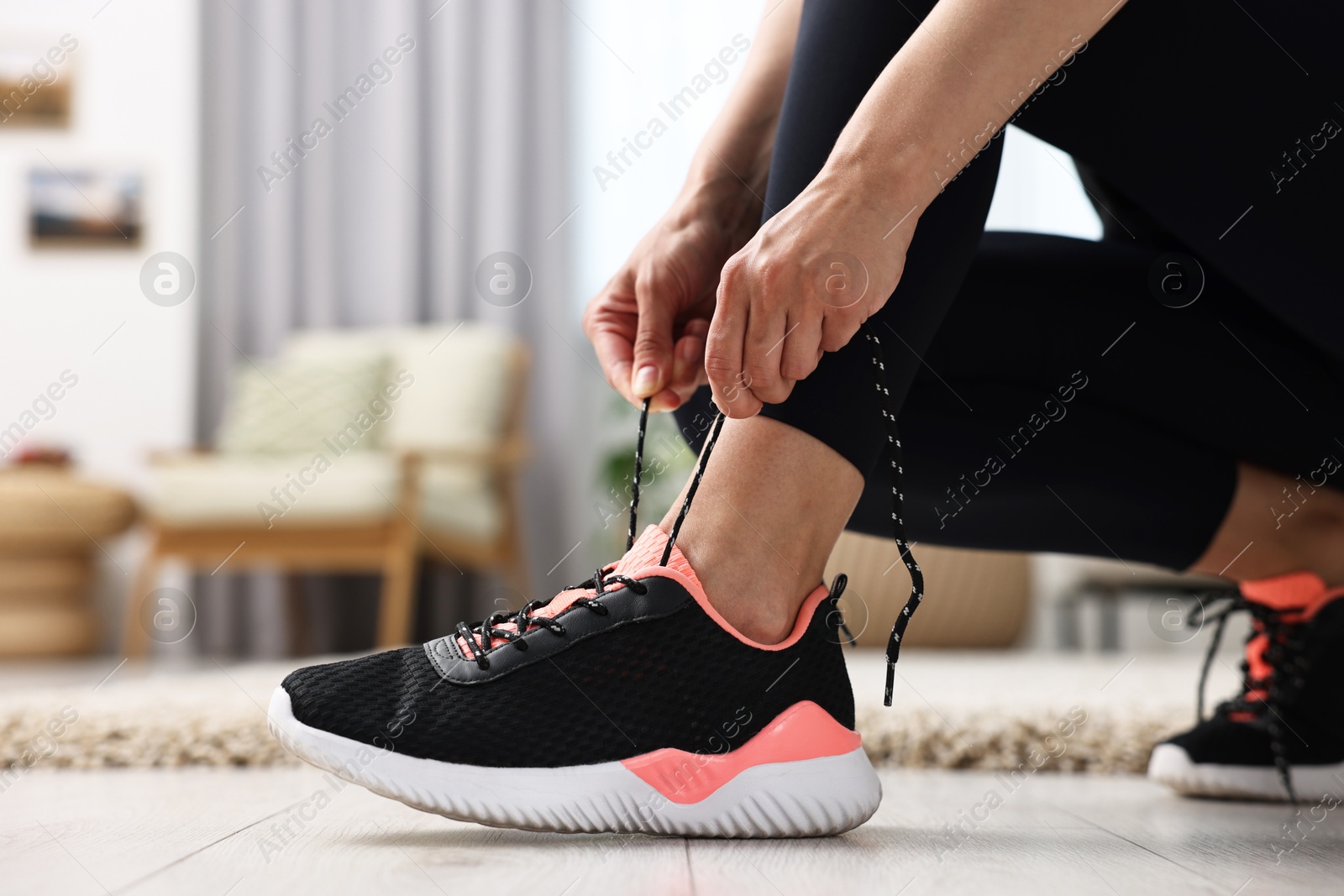 Photo of Woman tying shoelace of sneaker indoors, closeup