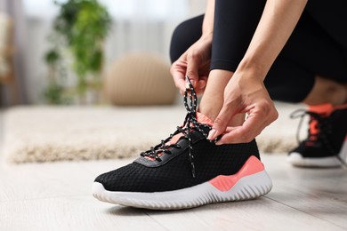 Woman tying shoelace of sneaker indoors, closeup