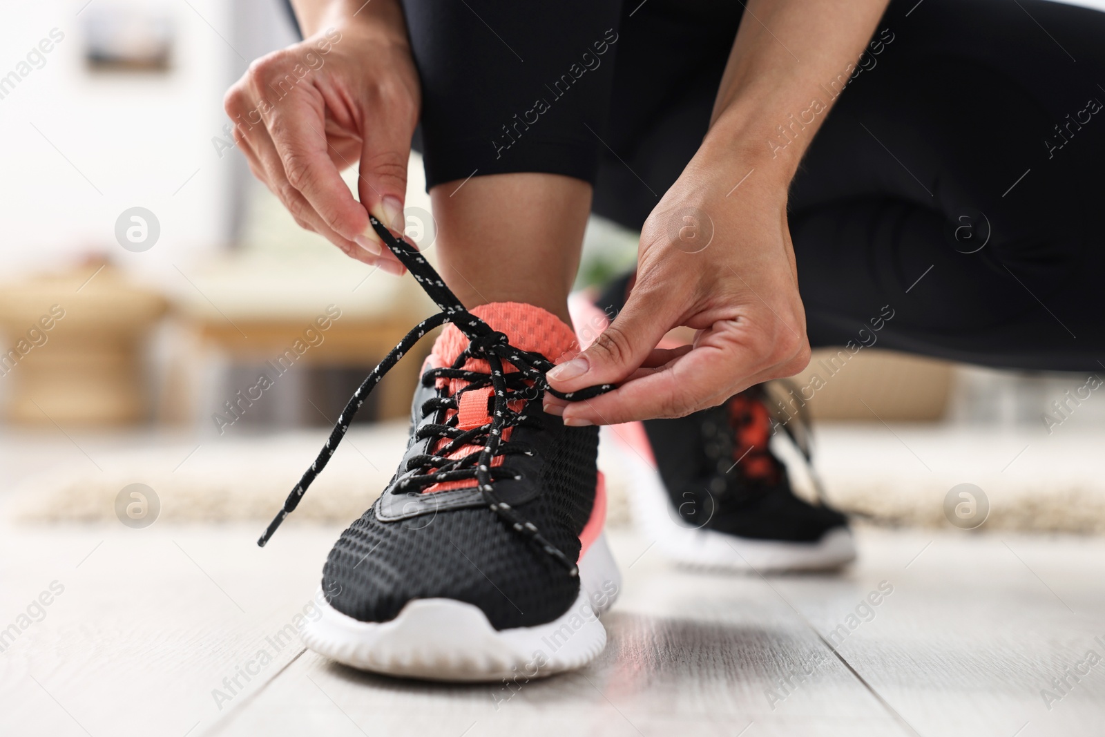 Photo of Woman tying shoelace of sneaker indoors, closeup