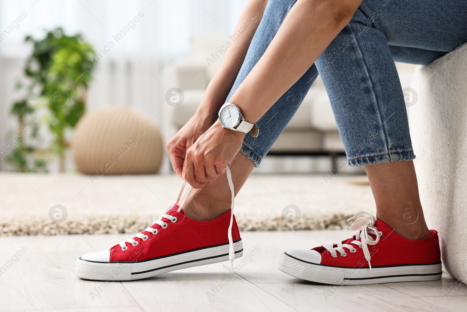 Photo of Woman tying shoelace of red sneaker indoors, closeup