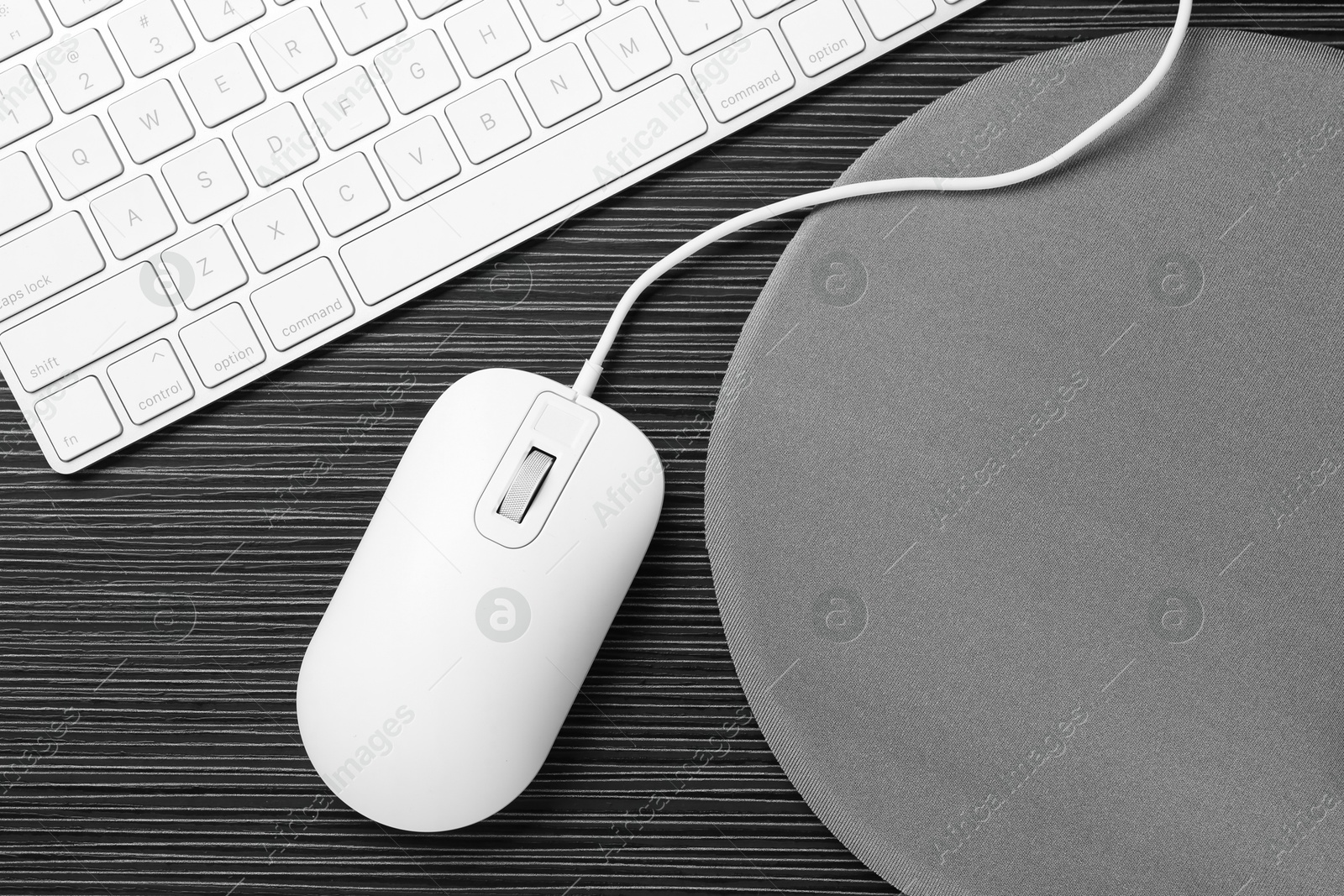 Photo of Computer mouse, mousepad and keyboard on black wooden table, flat lay