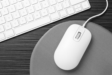 Photo of Computer mouse, mousepad and keyboard on black wooden table, flat lay