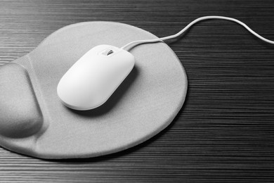 Photo of Computer mouse and mousepad with armrest on black wooden table