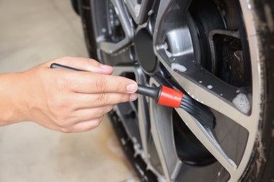 Photo of Man cleaning car wheel with brush indoors, closeup