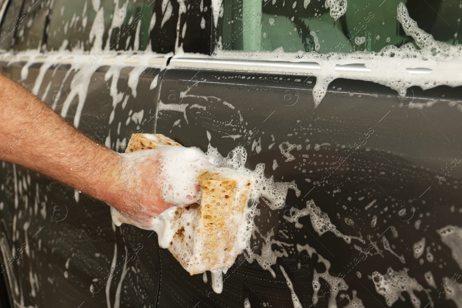 Photo of Man washing auto with sponge at car wash, closeup