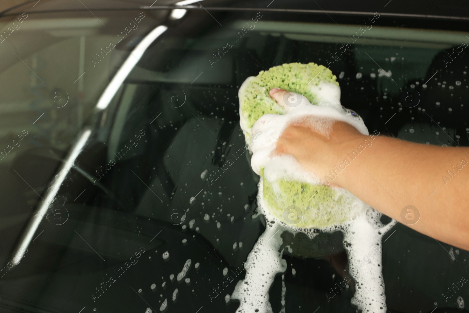 Photo of Man washing car windshield with sponge indoors, closeup