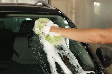 Man washing car windshield with sponge indoors, closeup