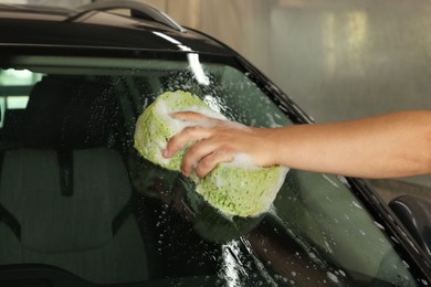 Photo of Man washing car windshield with sponge indoors, closeup