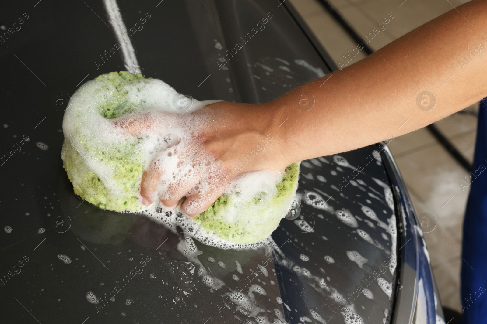 Photo of Man washing car hood with sponge indoors, closeup