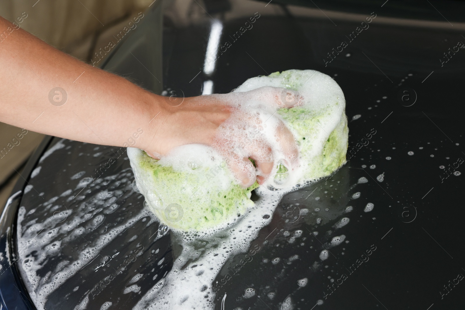 Photo of Man washing car hood with sponge indoors, closeup