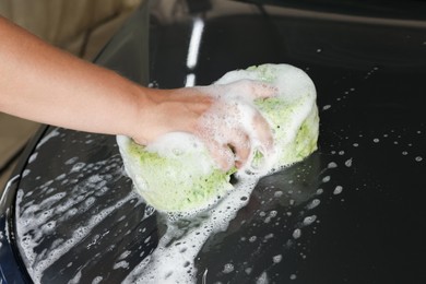 Man washing car hood with sponge indoors, closeup