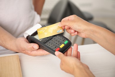 Photo of Man taking payment from client via credit card terminal at white wooden table, closeup