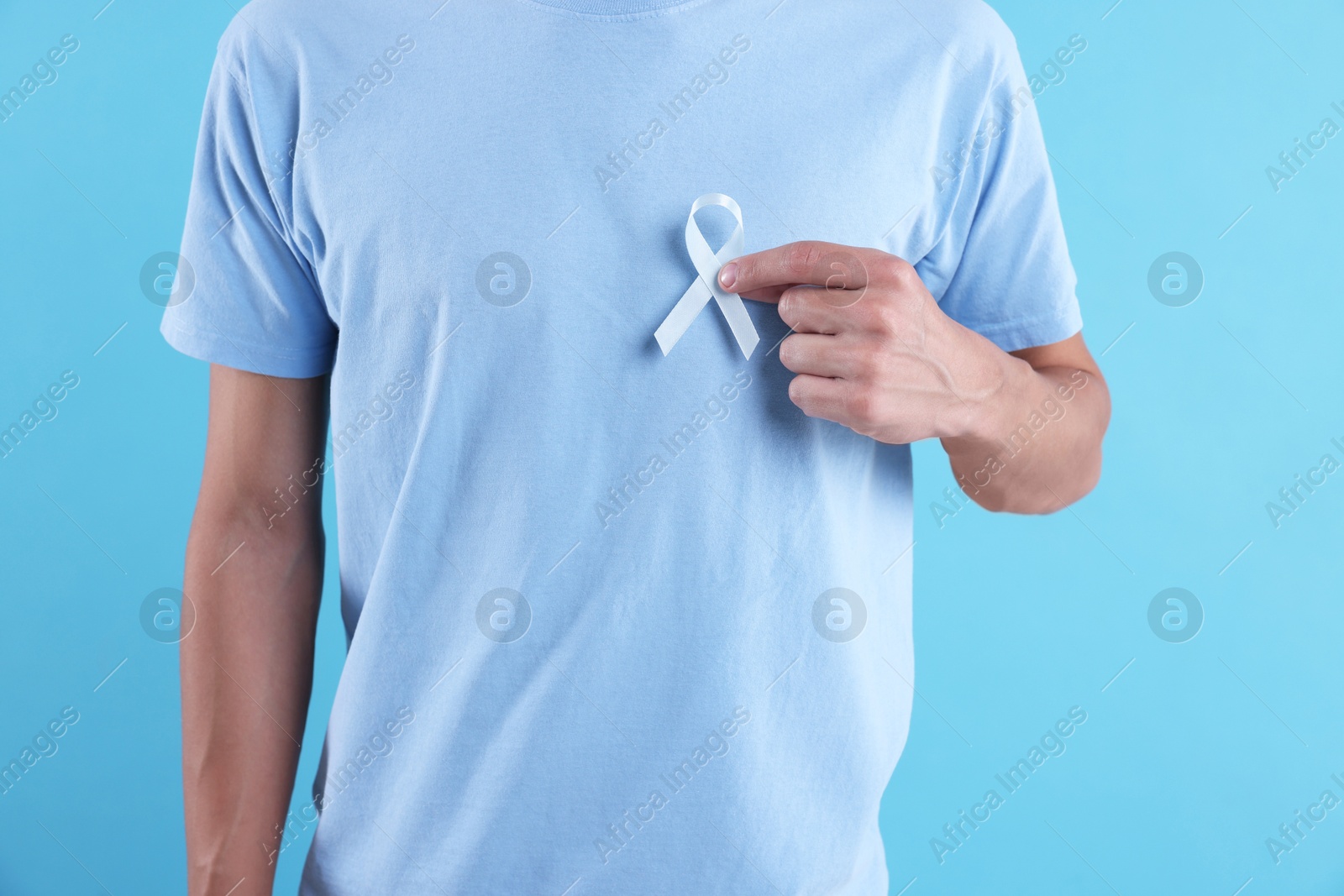 Photo of Prostate cancer awareness. Man with light blue ribbon as symbol of support on color background, closeup