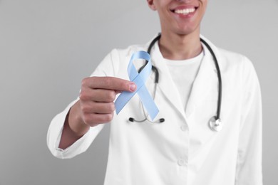 Photo of Prostate cancer awareness. Doctor holding light blue ribbon as symbol of support on grey background, selective focus